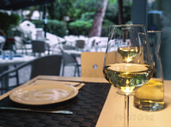 A glass and a carafe of white wine on a table in a street cafe and tableware