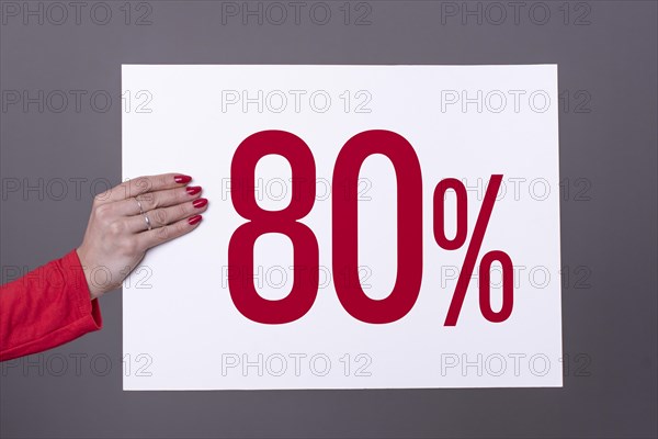 Female hand holding a 80% poster. Studio shot. Commercial concept