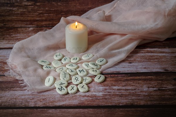 Viking stone runes on a pink silk cloth with a white candle on a wooden table