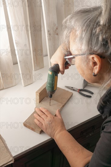 Woman seen in profile with an electric screwdriver putting screws into a piece of wood