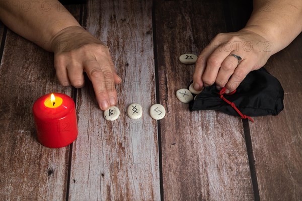 Woman reading the future with Viking runes with a red candle burning on a wooden table