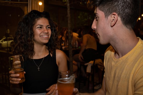Young latina woman smiling and chatting with a young man in a bar drinking beer. Meeting of an online date. Blurred background