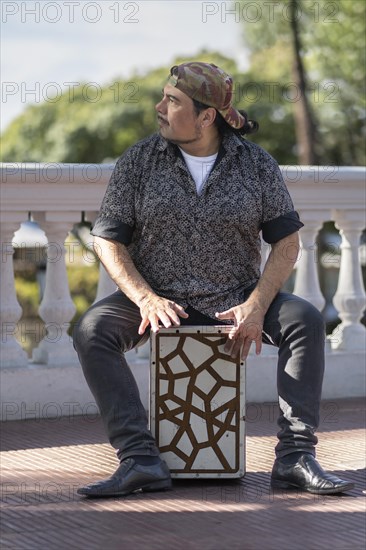 Hispanic man shot hands playing percussion with a Flamenco box sitting on top of it in a park