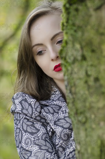 Thoughtful young woman standing behind a tree