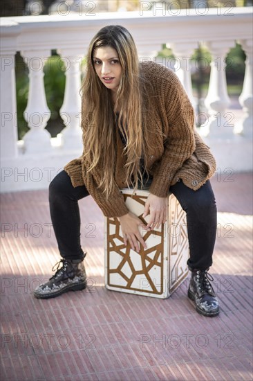 Woman shot hands playing percussion with a Flamenco box sitting on top of it in a park