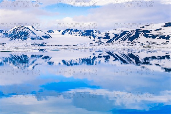Rocky coastline with snow-capped mountains reflecting in the water in a wild landscape in the Arctic