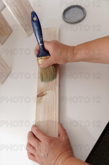 Woman's hands painting white on a wooden board with a paintbrush