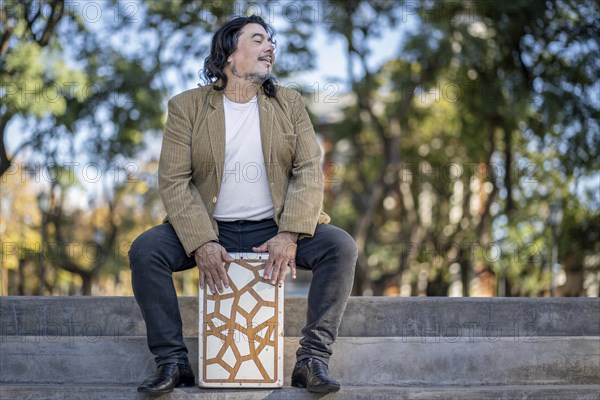 Hispanic man shot hands playing percussion with a Flamenco box sitting on top of it in a park
