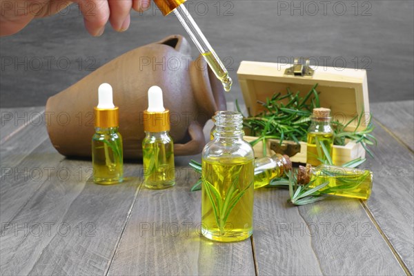 Close-up of a dropper with a drop of rosemary oil in the background several bottles of rosemary essence in a wooden box