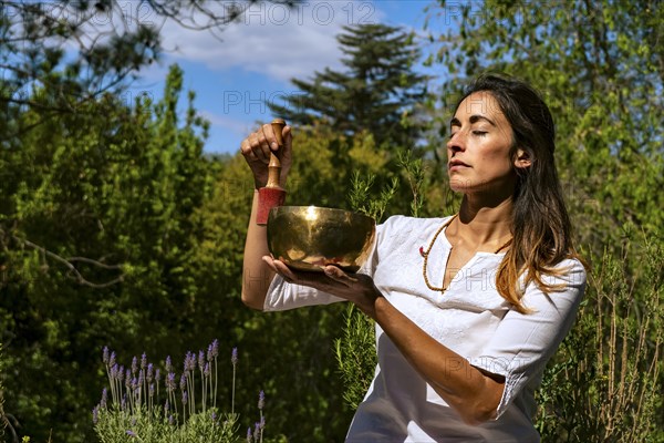 Young woman feeling the vibration of a Tibetan singing bowl outdoors. Sound therapy and meditation