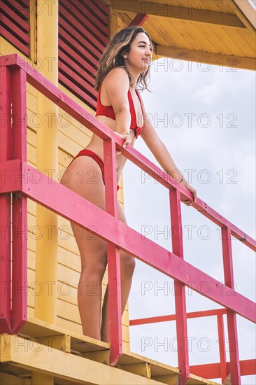 Beautiful tanned young woman standing in red bikini looking at horizon