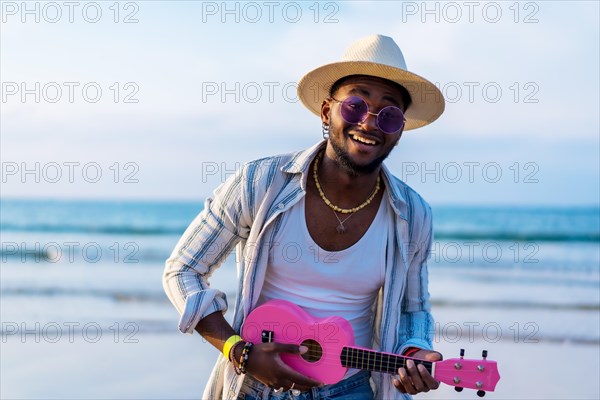 Black ethnic man playing ukulele by the sea enjoying summer vacation on the beach