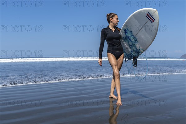 Young woman with prosthesis on her leg competes in adapted surfing. Sea out of focus in the background