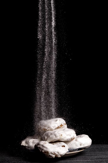 Glazed sugar doughnuts with icing sugar falling on them with black background and copy space