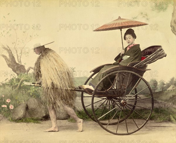A distinguished woman with a parasol being pulled in a jinrikisha by a man wearing a straw mackintosh