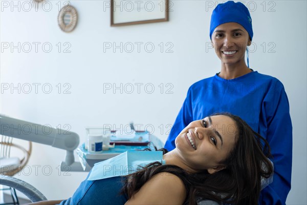 Beautiful young woman smiles sitting in the dentist's chair. She and her doctor look at the camera happy with the result of orthodontic treatment