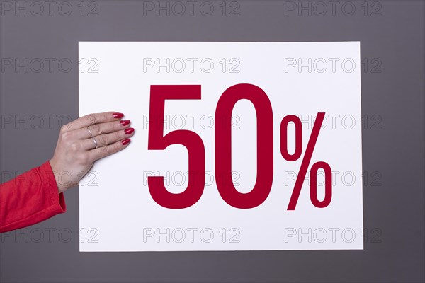 Female hand holding a 50% poster. Studio shot. Commercial concept