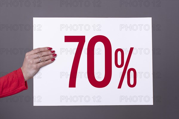 Female hand holding a 70% poster. Studio shot. Commercial concept