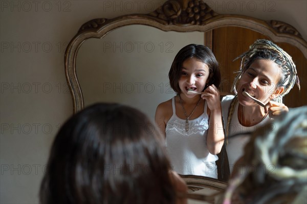 Mother teaches her daughter how to brush her teeth. Image reflected in the bathroom mirror