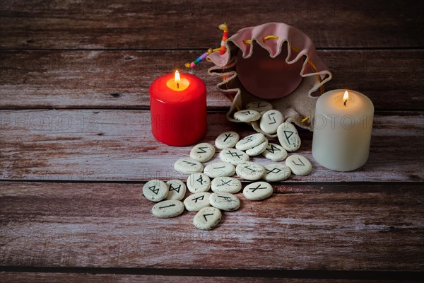 Viking stone runes from his pink leather sack with two candles on a wooden table