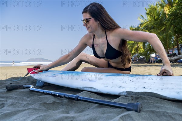 Una surfista femenina haciendo los ajustes finales a su tabla antes de una competencia de surf adaptado. Cancer survivor. Concept of disability in sport