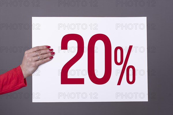 Female hand holding a 20% poster. Studio shot. Commercial concept