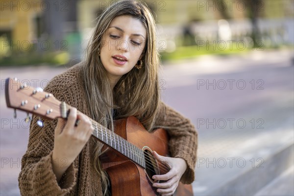 Young blonde woman playing the guitar and singing in the street