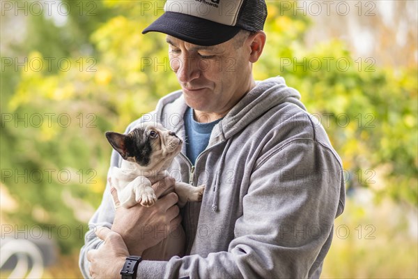 A man hugging a charming french bulldog puppy. Both looking at each other