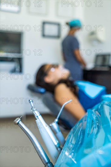 Dentist tools and equipment in foreground and patient and dentist out of focus in background