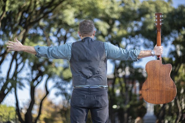 Guitarist in a park posing backwards holding his guitar with one hand