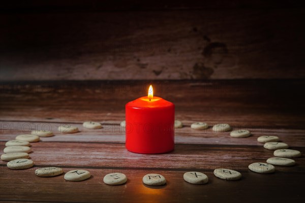 Circle of Viking stone runes on a wooden table with a lighted red candle in the center