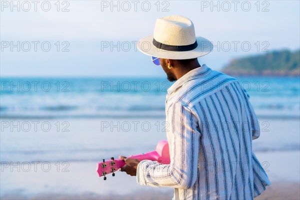 Portrait of black ethnic man enjoy summer vacation on the beach playing ukulele by the sea