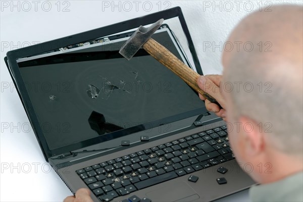 Angry man seen in profile breaking a laptop with a hammer