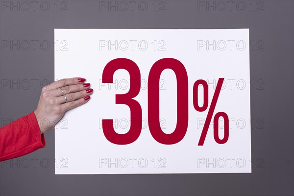 Female hand holding a 30% poster. Studio shot. Commercial concept