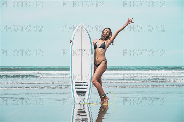 Beautiful young latin woman in bikini and with black surfboard. The woman is on the beach. Holiday and summer concept