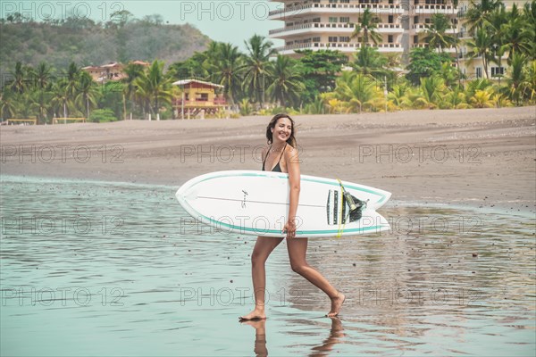 Beautiful young latina with surfboard on the shore walking towards the sea. Holiday and summer concept. Concept of healthy and active life