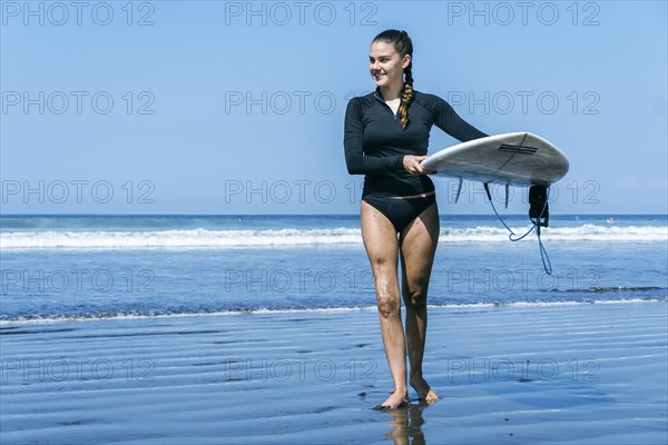 Inclusivity in sports: A young woman with a prosthesis emerging from the sea with her surfboard