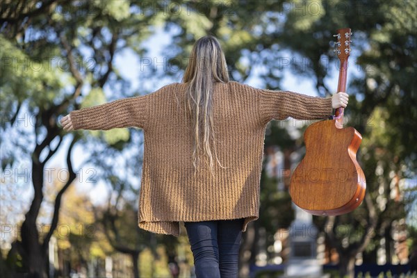 Guitarist in a park posing backwards holding his guitar with one hand