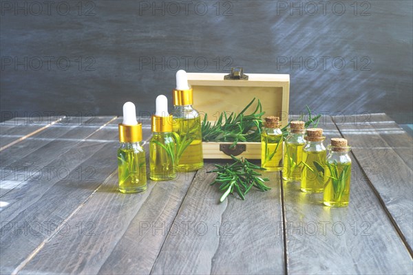 Bottles in a row with droppers of rosemary essential oil with a wooden box and fresh rosemary branches