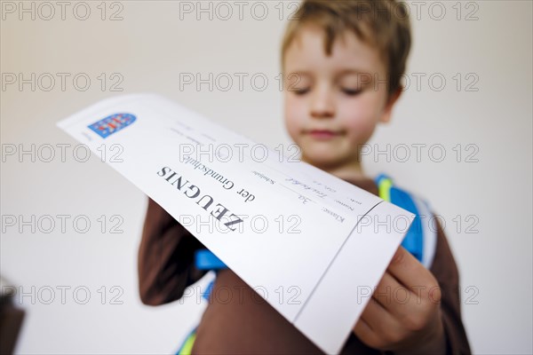 Symbolic photo on the subject of report cards in primary school. A boy poses with a report card. Berlin