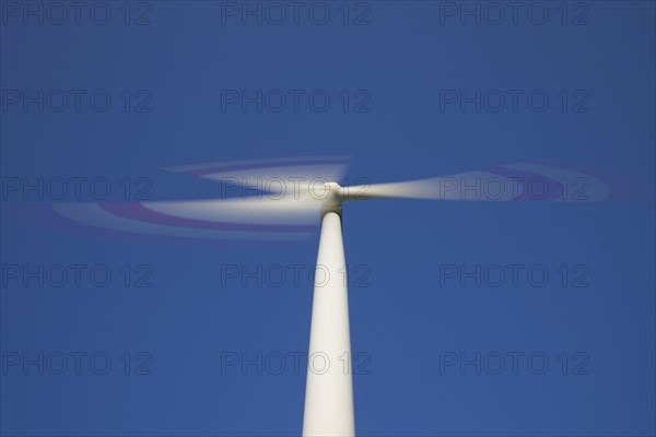 Worm's eye view on spinning blades of wind turbine against blue sky