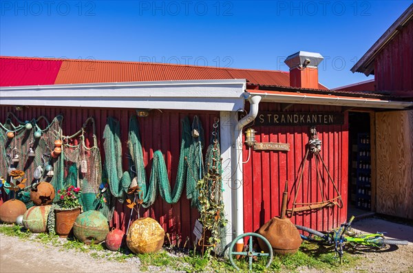 Discarded maritime objects and equipment such as rusty buoys and old fishing nets displayed on the wooden wall of a shed