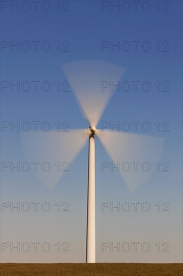 Spinning blades of windturbine in field against blue sky