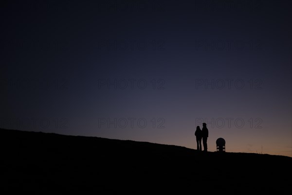 Two people silhouetted in front of the Teufelsberg in Berlin