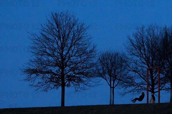 A person on a swing is silhouetted at blue hour