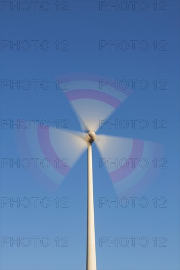 Spinning blades of wind turbine against blue sky