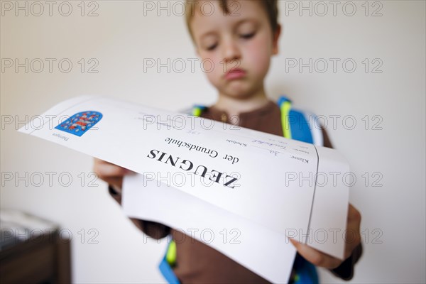 Symbolic photo on the subject of report cards in primary school. A boy poses with a report card. Berlin