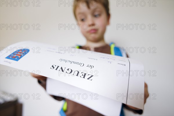 Symbolic photo on the subject of report cards in primary school. A boy poses with a report card. Berlin