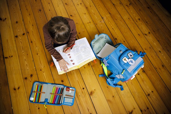 Symbolic photo on the subject of doing homework at home. A boy sits on the floor doing homework. Berlin