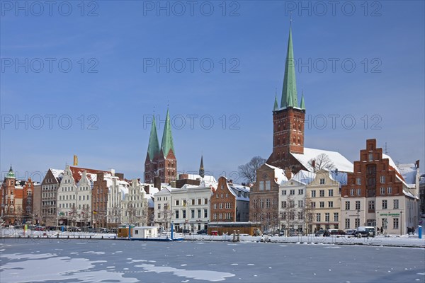 The churches of Saint Petri and Saint Mary towering above historic houses along the frozen river Trave in Luebeck in winter